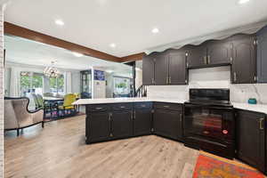 Kitchen featuring black electric range, a peninsula, decorative backsplash, light wood finished floors, and recessed lighting