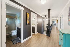 Hallway with light wood-style flooring, ornamental molding, an upstairs landing, and a chandelier