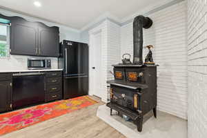 Kitchen with black appliances, crown molding, light wood-style flooring, a wood stove, and brick wall