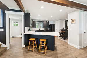 Kitchen with a kitchen bar, dark cabinetry, ornamental molding, beamed ceiling, and a peninsula