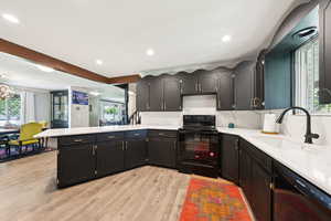 Kitchen with healthy amount of natural light, a peninsula, black appliances, light wood-type flooring, and recessed lighting