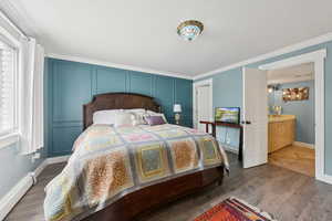 Bedroom with a baseboard heating unit, ornamental molding, and wood finished floors