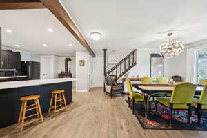 Dining area featuring a wood stove, crown molding, stairway, light wood-style flooring, and beam ceiling