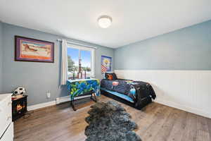 Bedroom featuring wood finished floors, a wood stove, baseboard heating, and a wainscoted wall