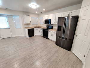 Kitchen featuring black appliances, white cabinets, light countertops, a textured ceiling, and light wood-type flooring
