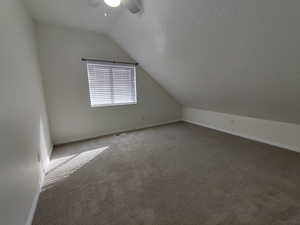Additional living space with vaulted ceiling, a textured ceiling, carpet flooring, and a ceiling fan