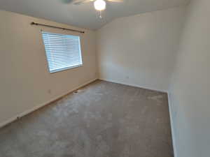 Carpeted empty room with lofted ceiling and a ceiling fan
