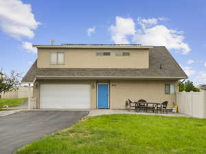 View of front facade featuring roof with shingles, stucco siding, an attached garage, a patio, and roof mounted solar panels
