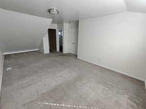 Unfurnished living room with vaulted ceiling, carpet floors, and a textured ceiling