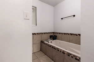Full bath featuring a jetted tub, light tile patterned floors, and a textured wall