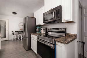 Kitchen featuring stainless steel appliances, dark countertops, white cabinetry, and wood finished floors