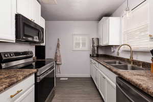 Kitchen featuring stainless steel electric range oven, white cabinetry, dark wood finished floors, dishwashing machine, and hanging light fixtures