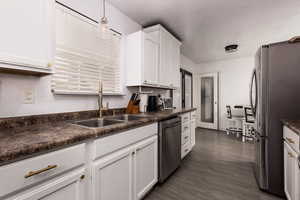 Kitchen featuring dark countertops, appliances with stainless steel finishes, dark wood finished floors, white cabinetry, and decorative light fixtures