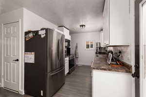 Kitchen featuring appliances with stainless steel finishes, white cabinetry, dark wood-type flooring, and a textured ceiling