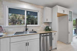 Kitchen with white cabinets, stainless steel dishwasher, tasteful backsplash, light stone counters, and light tile patterned floors