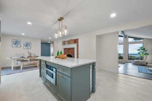Kitchen with decorative light fixtures, a center island, light stone counters, stainless steel oven, and recessed lighting