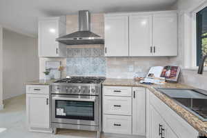 Kitchen with wall chimney exhaust hood, white cabinets, stainless steel range, and backsplash