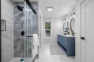 Bathroom with light marble finish floors, double vanity, a marble finish shower, tile walls, and a textured ceiling