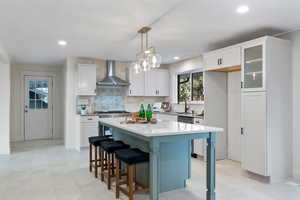 Kitchen featuring a kitchen breakfast bar, a center island, glass insert cabinets, backsplash, and hanging light fixtures