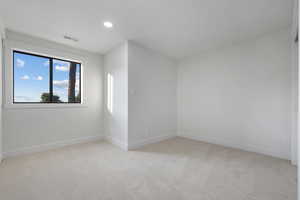 Empty room with light colored carpet and recessed lighting