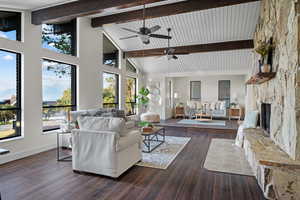 Living room with a stone fireplace, high vaulted ceiling, dark wood finished floors, beam ceiling, and ceiling fan
