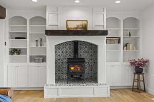 Living room with a wood stove, built in features, light wood finished floors, and recessed lighting