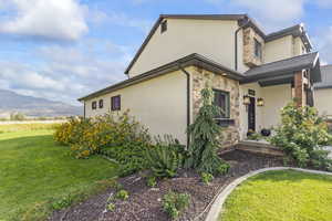 View of front of home with stone siding, a front lawn, stucco siding, and a mountain view