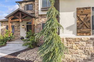 Entrance to property with stone siding, stucco siding, and a porch