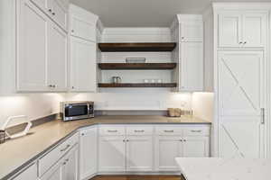 Kitchen featuring white cabinets, open shelves, light stone counters, and stainless steel microwave