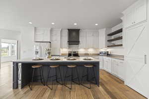 Kitchen with white cabinets, a breakfast bar area, a large island, light wood finished floors, and recessed lighting