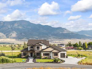 View of front of house featuring stone siding, concrete driveway, a mountain view, a garage, and a view of rural / pastoral area