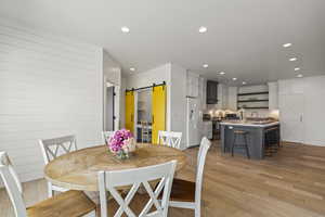 Dining area with a barn door, light wood-style floors, and recessed lighting