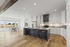 Kitchen with a kitchen breakfast bar, white cabinetry, light wood finished floors, recessed lighting, and an island with sink