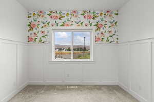 Unfurnished dining area featuring a decorative wall, wainscoting, and light colored carpet