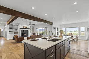 Kitchen with beam ceiling, recessed lighting, a fireplace, light stone countertops, and light wood-type flooring