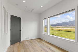 Empty room with a mountain view, recessed lighting, light wood-style flooring, and attic access