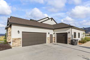 View of home's exterior with stone siding, concrete driveway, a mountain view, stucco siding, and an attached garage