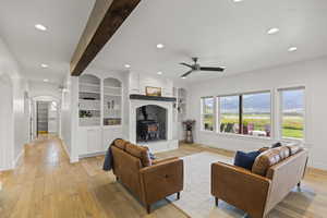 Living room featuring beam ceiling, a wood stove, recessed lighting, light wood-style floors, and arched walkways