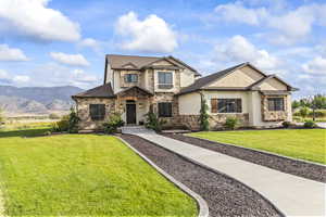 Craftsman-style house featuring a front lawn, stone siding, a mountain view, and stucco siding