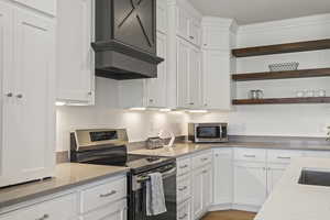 Kitchen with appliances with stainless steel finishes, white cabinetry, open shelves, light stone counters, and custom exhaust hood