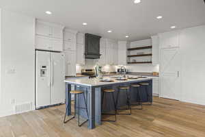 Kitchen with white cabinetry, white fridge with ice dispenser, a breakfast bar area, light wood-style floors, and an island with sink