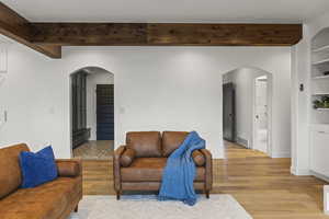 Living room featuring arched walkways, light wood-style flooring, built in shelves, and beamed ceiling