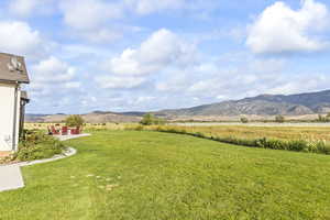 View of green lawn featuring a patio area, a mountain view, and a rural view