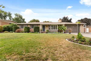 Single story home featuring brick siding, a front yard, a garage, and a chimney