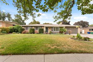 Single story home with a front lawn, a chimney, an attached garage, and driveway