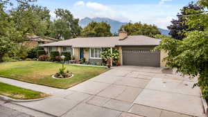 Ranch-style house featuring a mountain view, driveway, a shingled roof, a front lawn, and brick siding