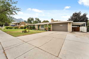 Ranch-style home featuring concrete driveway, a carport, a front lawn, brick siding, and a chimney