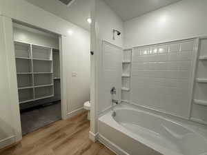 Full bath featuring washtub / shower combination, light wood-style floors, and a walk in closet