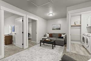 Living room with washing machine and dryer, light colored carpet, and a textured ceiling