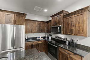 Kitchen featuring appliances with stainless steel finishes, dark stone countertops, dark brown cabinetry, and recessed lighting
